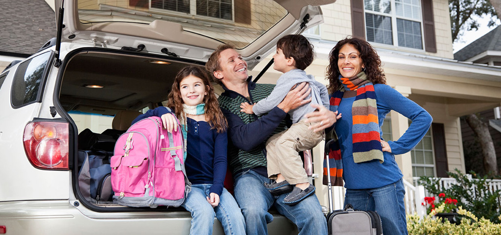 A happy family posing next to the back of their car